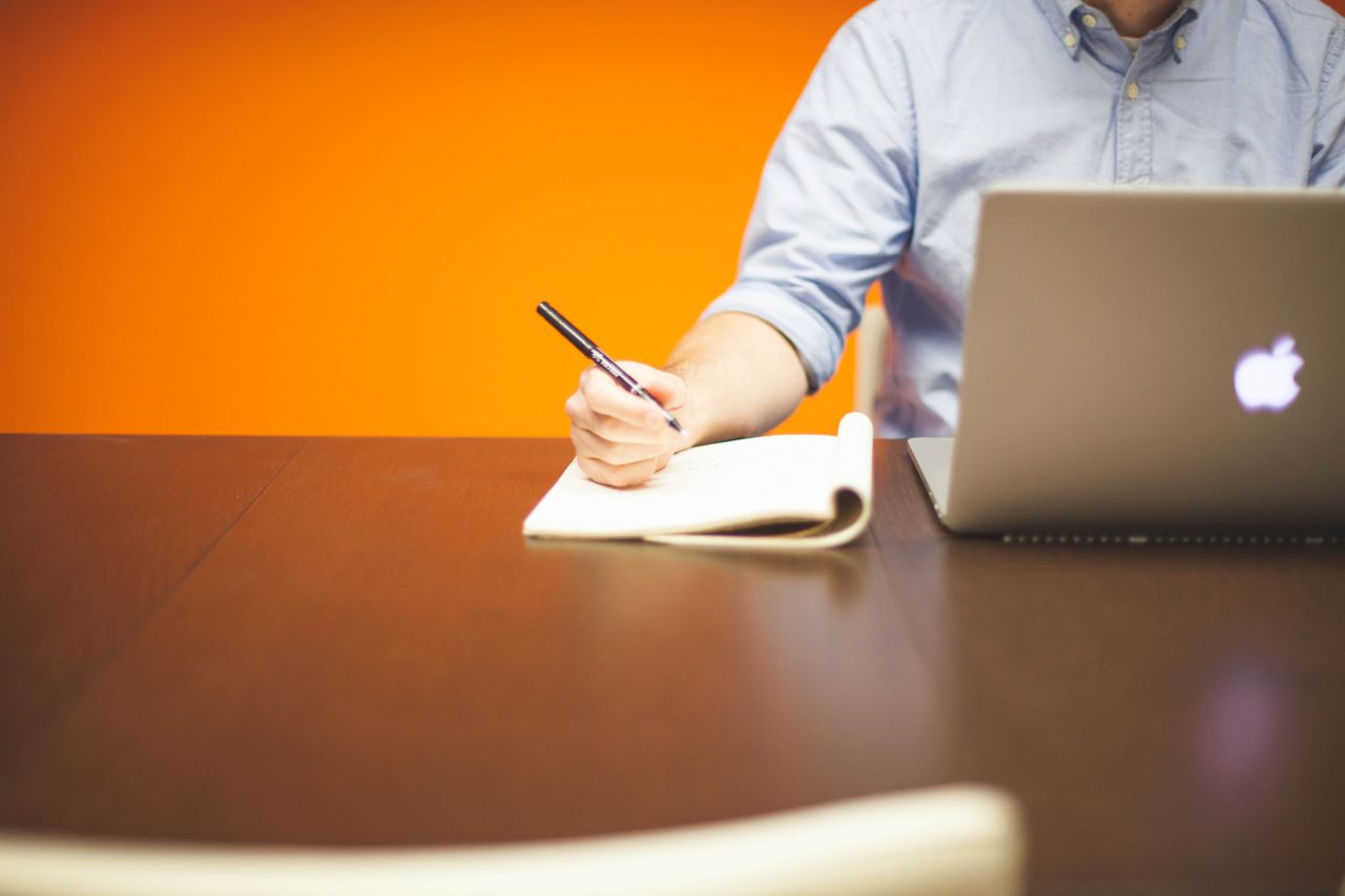 writing on a notepad while working on a laptop